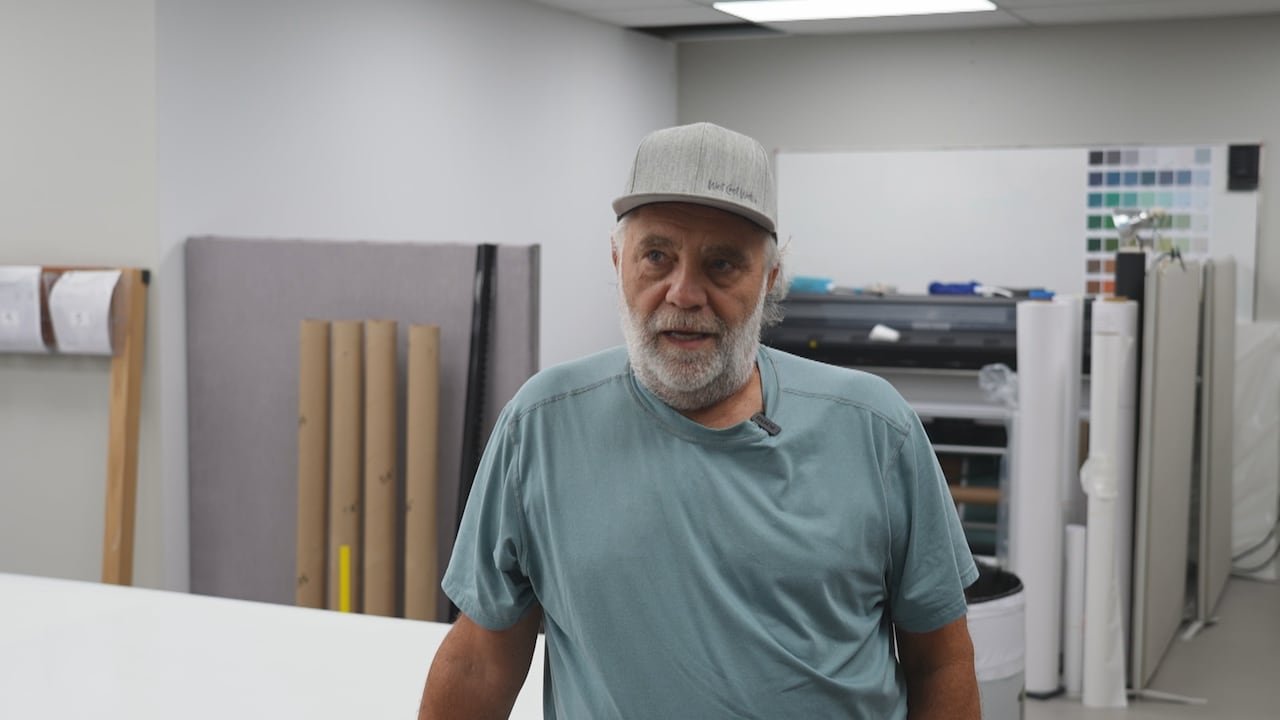 default-508 A man wearing a baseball cap and beard with wallpaper rolls in the background.