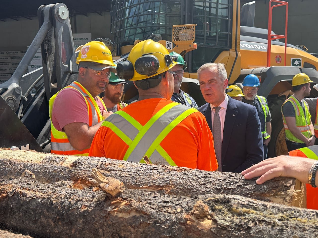 default-509 A man in a suit addressing mill workers wearing hard hats surrounded by logs.
